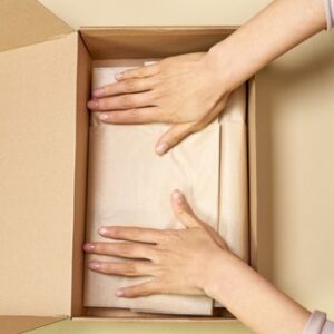 Close-up of hands packing a cardboard box with care using parchment paper.